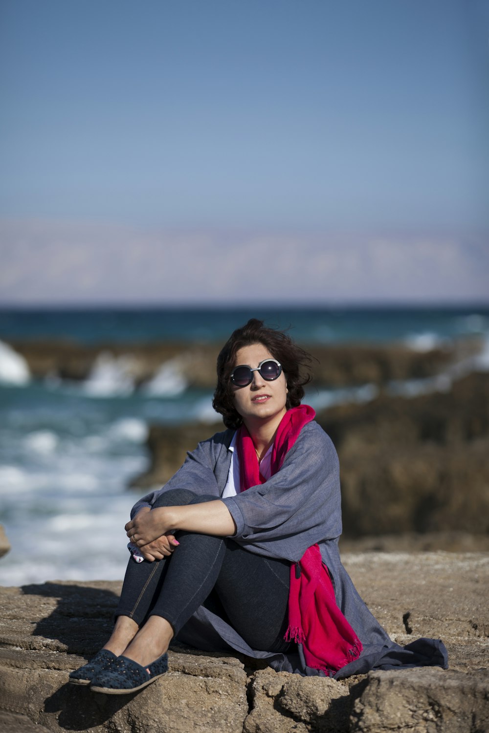 smiling woman seated on rock formation near body of water during daytime