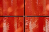 Four glossy red tiles with a slightly textured surface, arranged in a grid pattern. The tiles have a shiny, reflective quality, creating an impression of depth and richness.