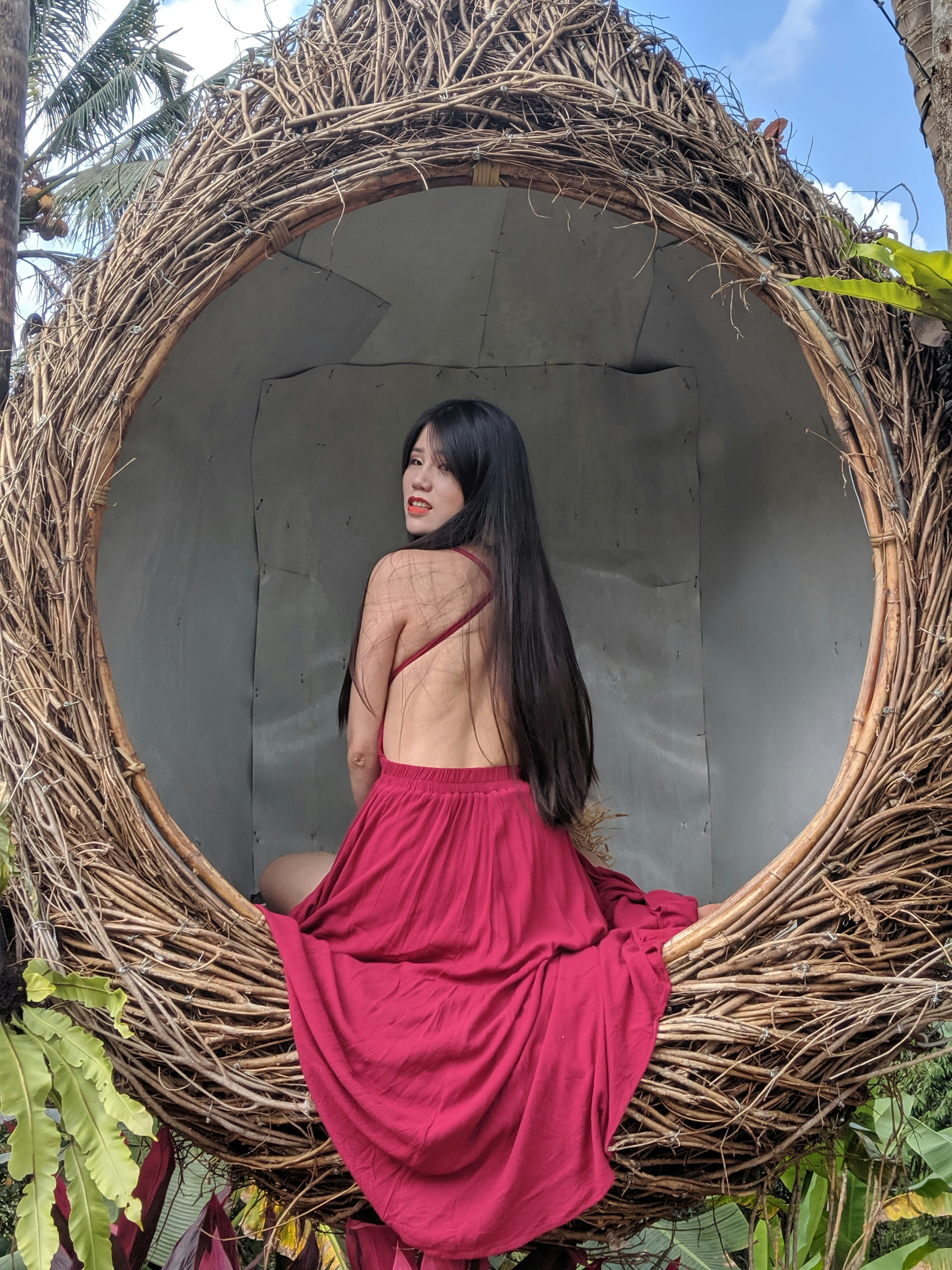 woman wearing pink backless dress sitting on brown hanging chair facing her left side