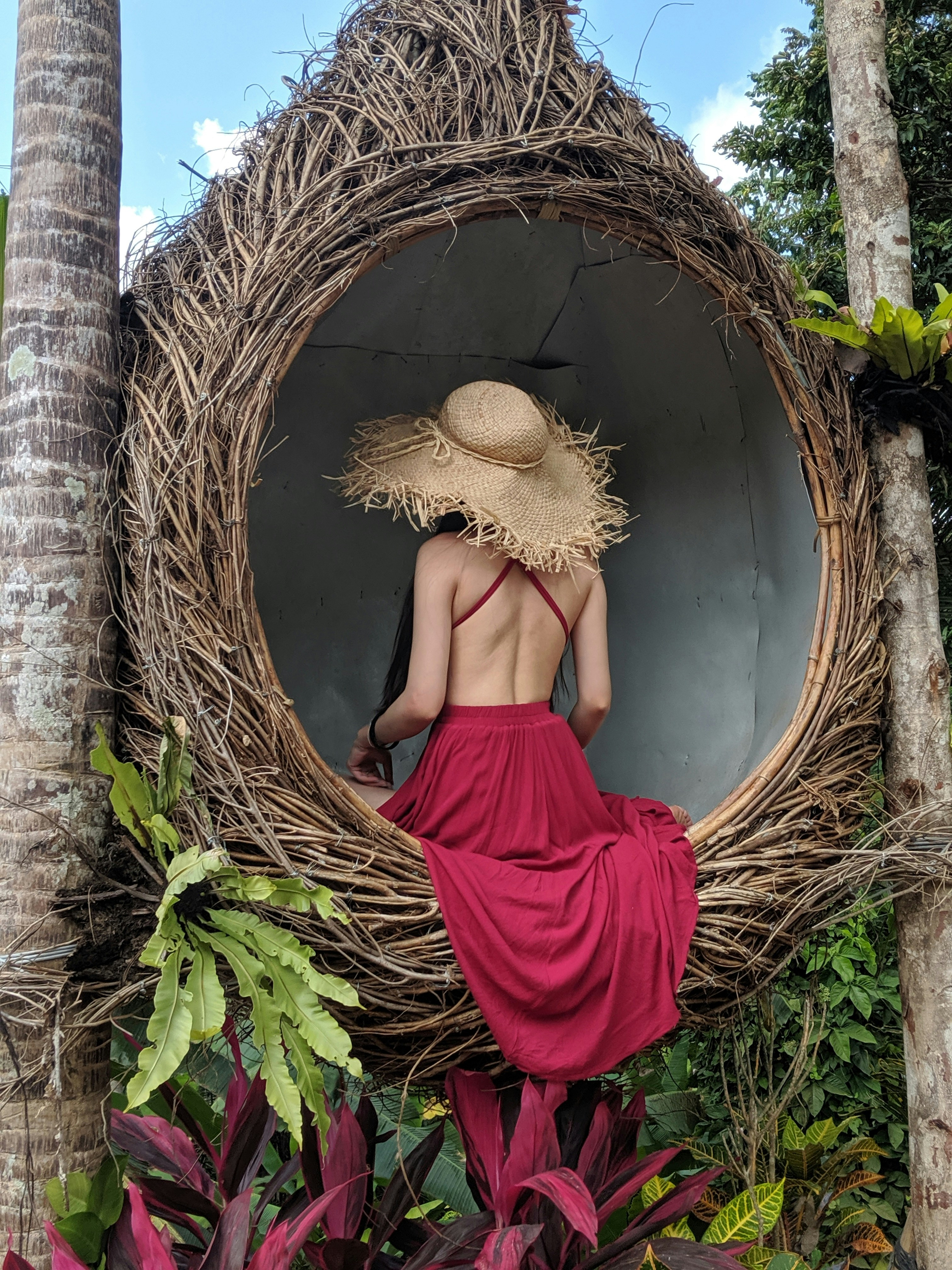 woman wearing pink backless dress sitting on wicker hanging chair