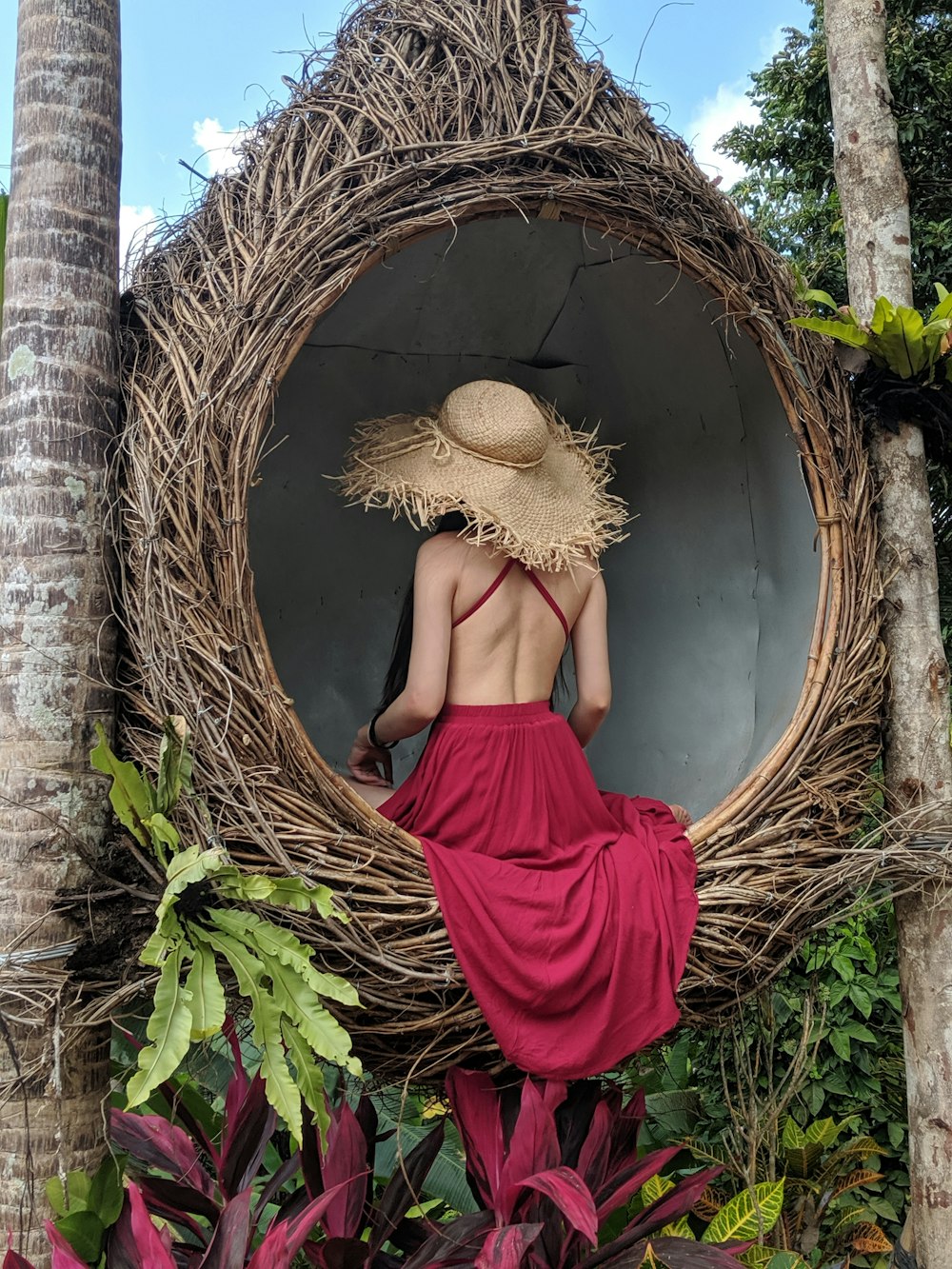 woman wearing pink backless dress sitting on wicker hanging chair