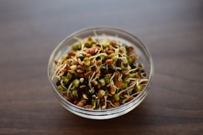 A beautifully arranged bowl of mixed sprouts topped with herbs and seeds on a rustic wooden table.