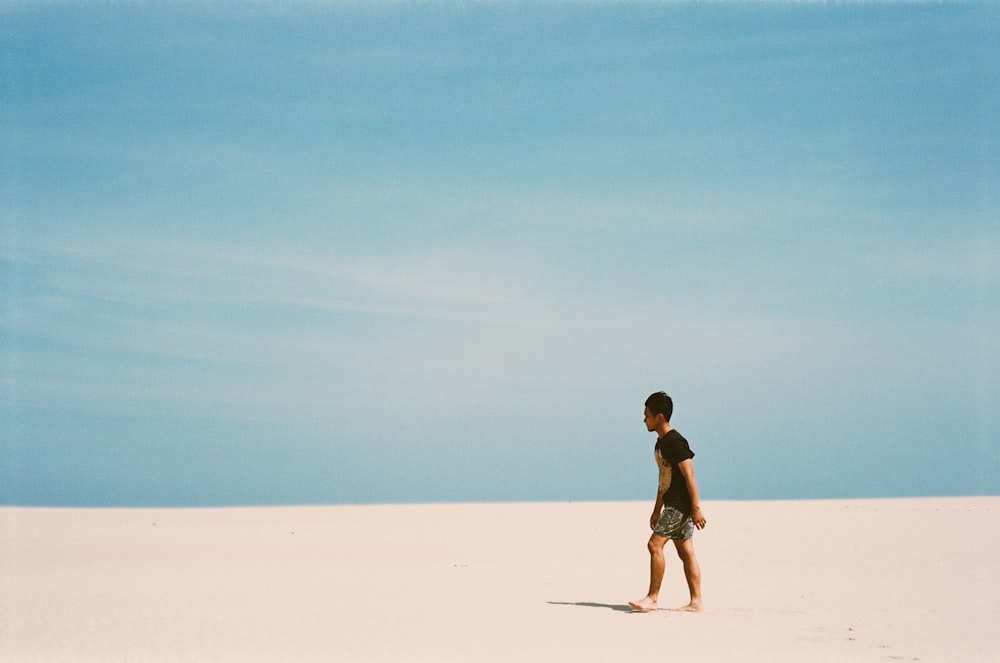 man wearing black shirt walking on white sand
