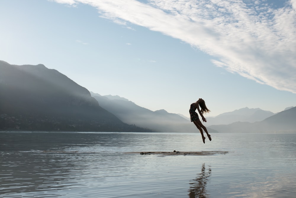 湖の真ん中でいかだの上でジャンプする女性のシルエット
