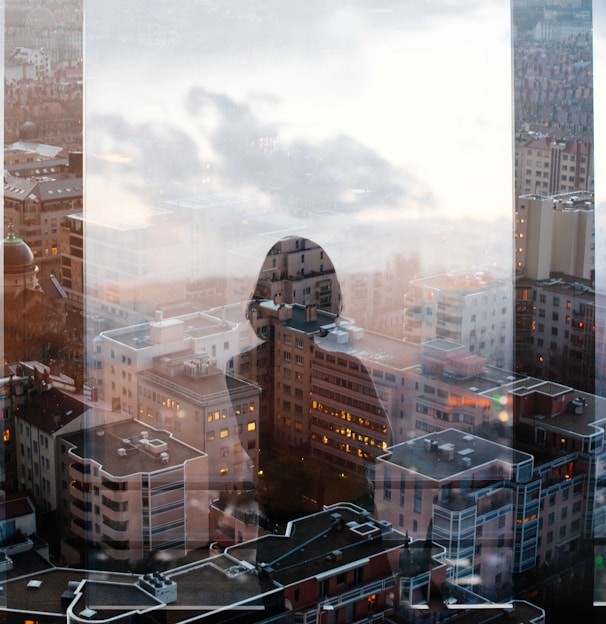 reflection of woman standing in front of glass panel facing high-rise and mid-rise buildings