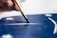 A close-up of a hand using a paintbrush to apply blue paint onto a surface, featuring white stars and stripes, suggesting a flag or patriotic theme.