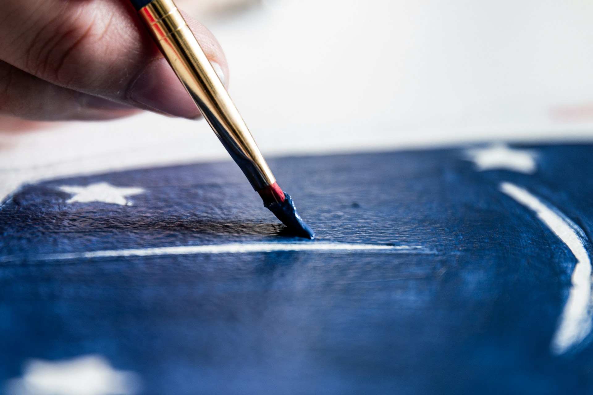 A close-up of a paintbrush applying a rich navy blue color on a decorative wall.