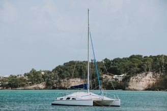 A sailboat anchored near a pristine New Zealand surf spot, with rolling hills and turquoise water in the background.