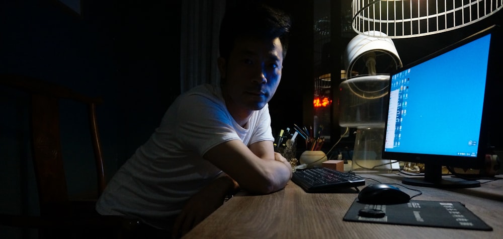 man leaning on brown wooden desk in front of turned-on flat screen monitor