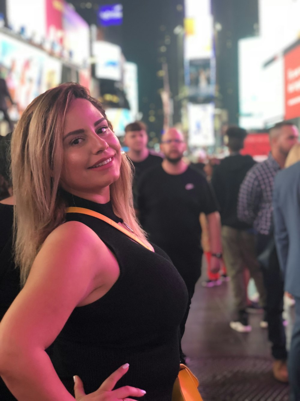 smiling woman in black tank top standing in middle of crowded city street at night