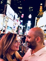 A happy pair taking a selfie with city lights sparkling behind them at night.
