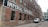 A long, red-brick industrial building with a painted sign 'IMPERIAL PAPER BOX CO.' along its side. The building features numerous black-framed windows and is set in an alleyway with parked vehicles, including a white van and a car.
