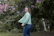 A joyful woman wearing a flowing bohemian blouse in muted sage, standing in a sunlit natural setting.