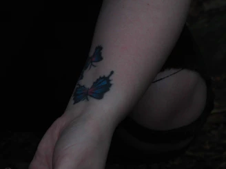 A close-up of a delicate fine line tattoo on a forearm, softly lit in a dark, luxurious studio setting.
