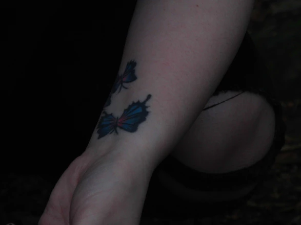 A close-up of a delicate fine line tattoo on a forearm, softly lit in a dark, luxurious studio setting.