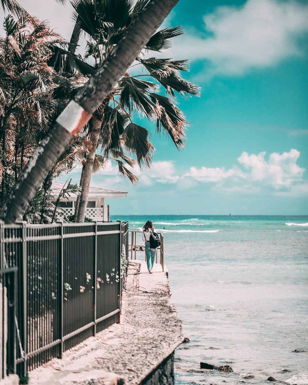 woman walking beside cottage and seashore during daytime