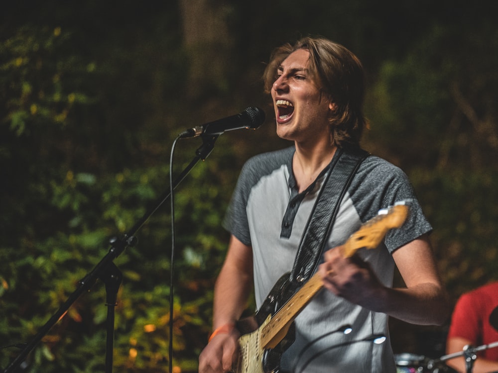 man wearing gray polo shirt playing electric guitar performing on stage