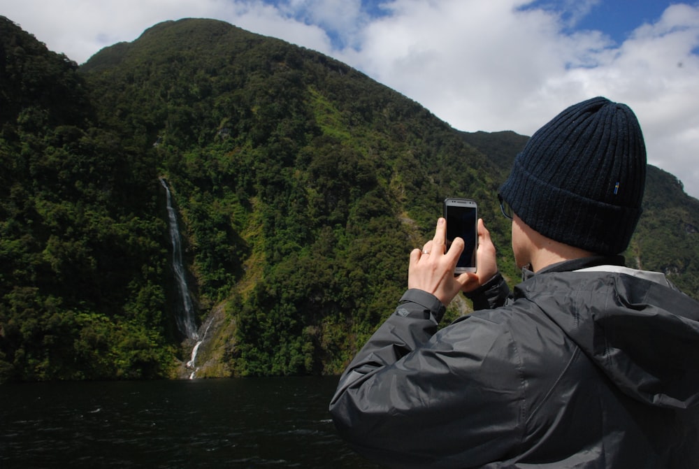 man in black jacket taking photo of waterfalls