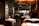 A sophisticated restaurant interior featuring neatly arranged tables with white tablecloths and elegant table settings. The walls are decorated with framed black-and-white art, adding to the refined ambiance. Warm lighting creates a cozy and inviting atmosphere. The restaurant appears spacious with a modern design, showcasing plush seating arranged in an orderly fashion.