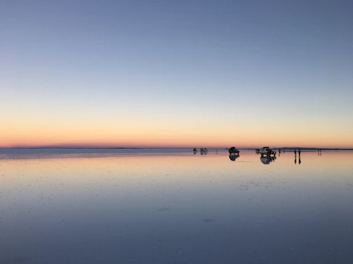Sunset over the endless reflective salt flats with tourists taking photos