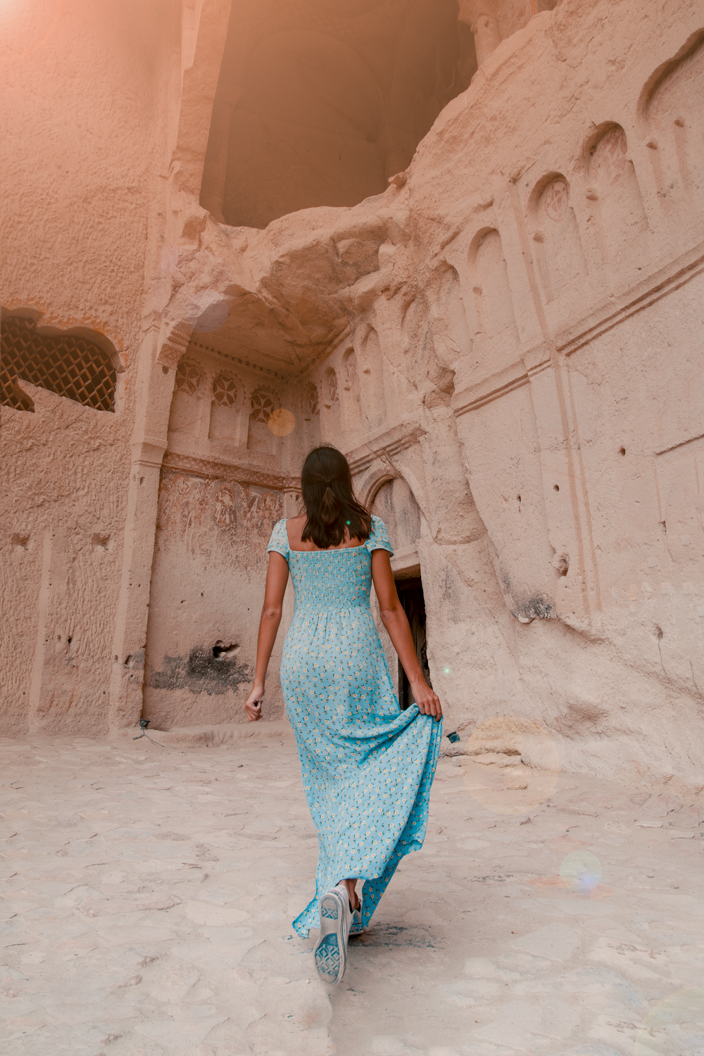 woman in teal dress walking by rock wall
