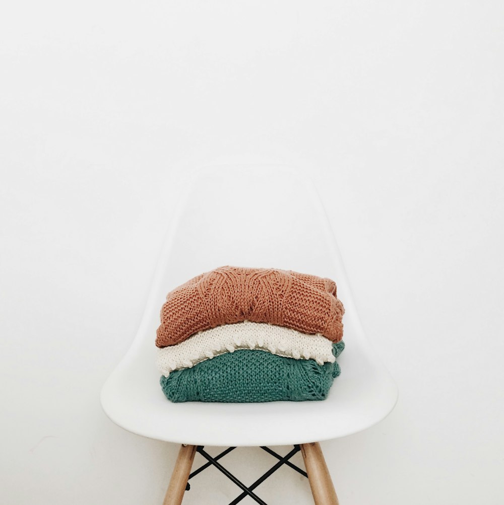 tre pile di vestiti lavorati a maglia su una sedia bianca