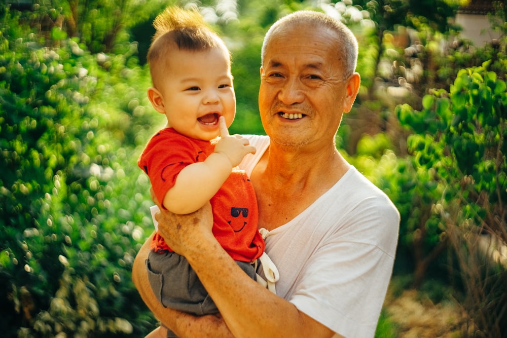 smiling man standing and carrying baby near green plants