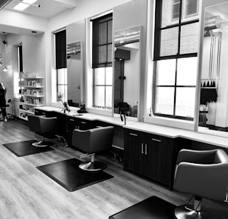 grayscale photo of woman using laptop near three salon chairs