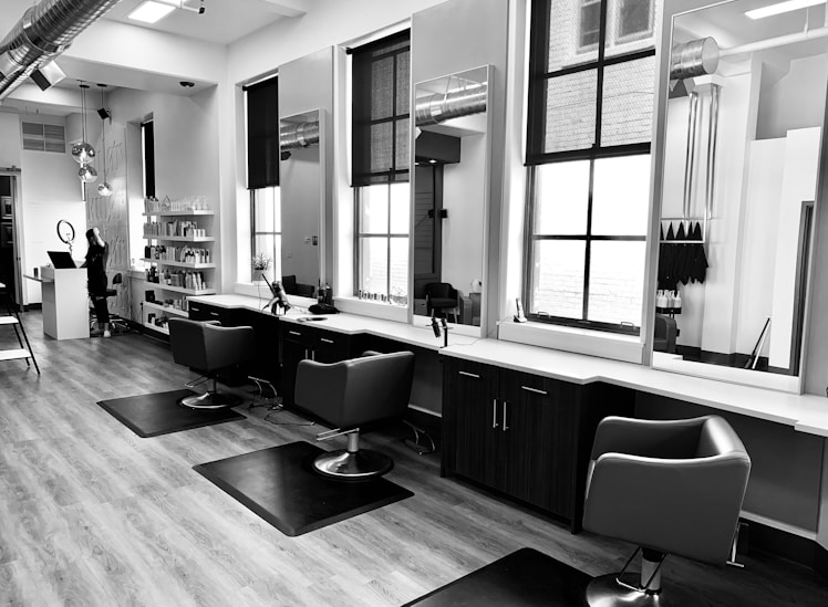 grayscale photo of woman using laptop near three salon chairs