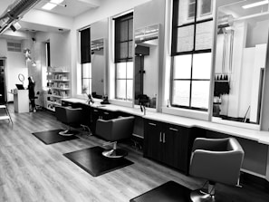 grayscale photo of woman using laptop near three salon chairs