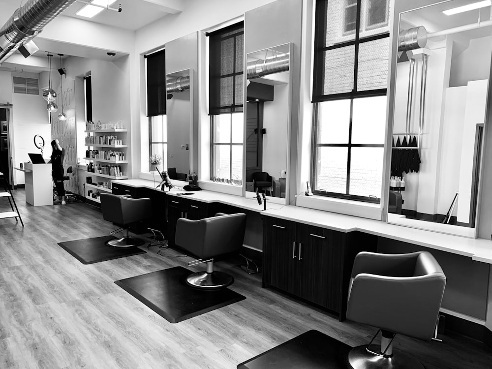 grayscale photo of woman using laptop near three salon chairs