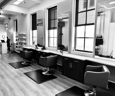 grayscale photo of woman using laptop near three salon chairs