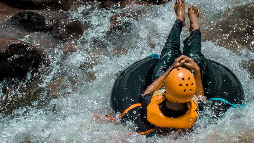 person riding inflatable pool ring on flowing body of water