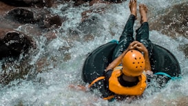 A person wearing a helmet and life jacket is sitting in an inflatable tube, navigating through rapids in a rocky river.