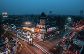 A panoramic view of a busy intersection framed by towering advertising screens illuminated at dusk.