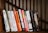 A person browsing through a collection of colorful books on a wooden shelf.