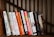 A person browsing through a collection of colorful books on a wooden shelf.