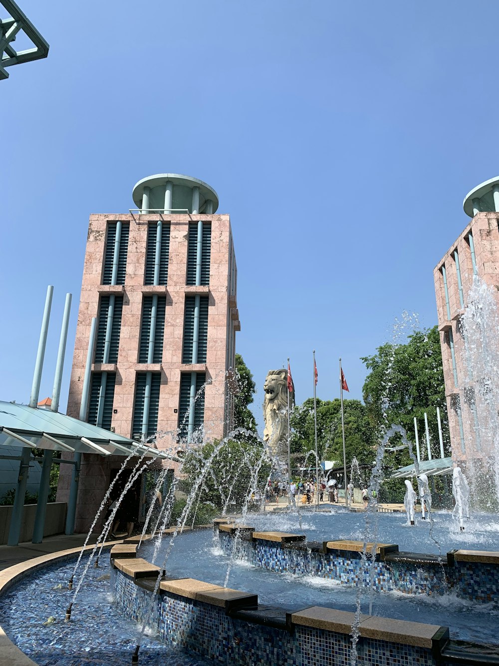 people walking near buildings beside water fountain under blue skies