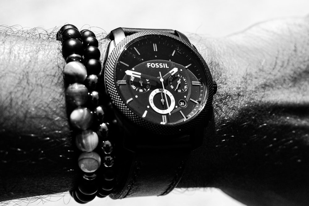 person wearing round Fossil chronograph watch with link band displaying 01:47 time