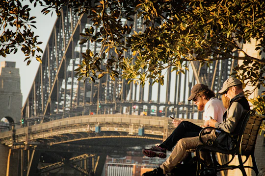 Two teenagers sitting on a park bench, animatedly discussing a story they just read on their phones.