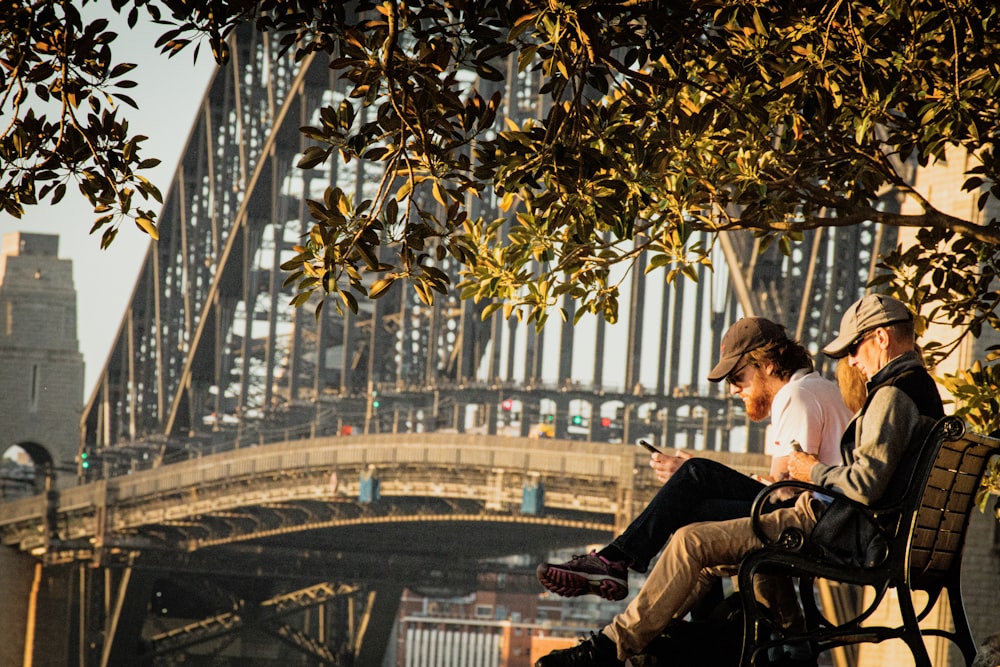 two men sitting beside brown and black bridge