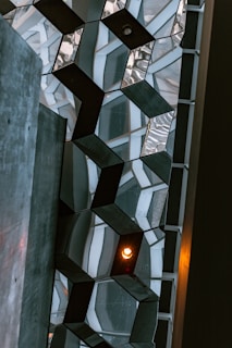 Architectural design with geometric patterns featuring hexagonal shapes made from a combination of glass and dark metal. A warm light bulb is visible among the hexagons, creating a striking contrast against the cool tones.