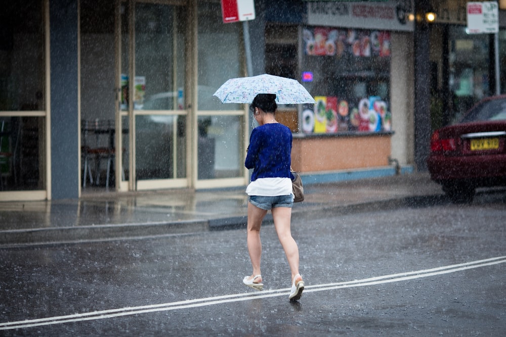 woman crossing on street holding umbrella