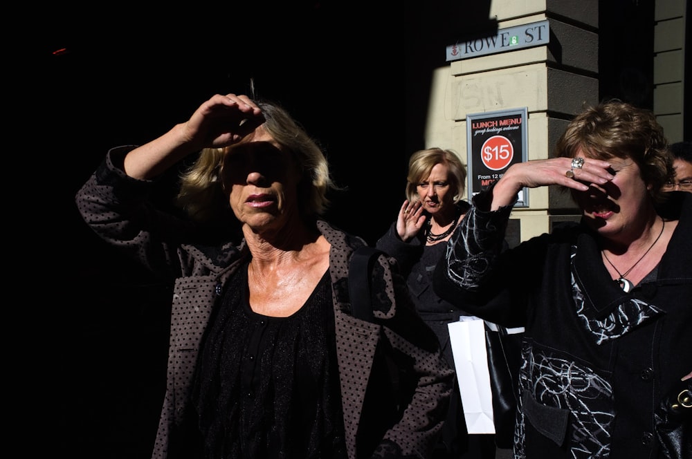 three women standing and covering face from sun light