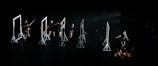 A group of dancers on a dark stage interacting with several geometric frames, each frame is lit emphasizing the performers' movements. The dancers are dressed in black, and their actions seem choreographed in a dynamic and expressive manner.