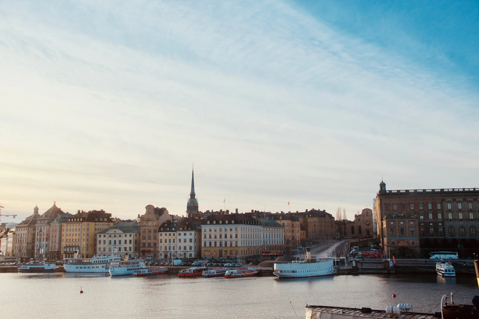 Stockholm waterfront in pale morning light, with boats moored along the quay and a church spire rising above the old town rooftops