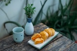 A small plate of lightly dusted pastries placed next to a warm cup of herbal infusion, surrounded by calming plants.