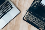 A close-up of hands typing on a classic typewriter beside a laptop.