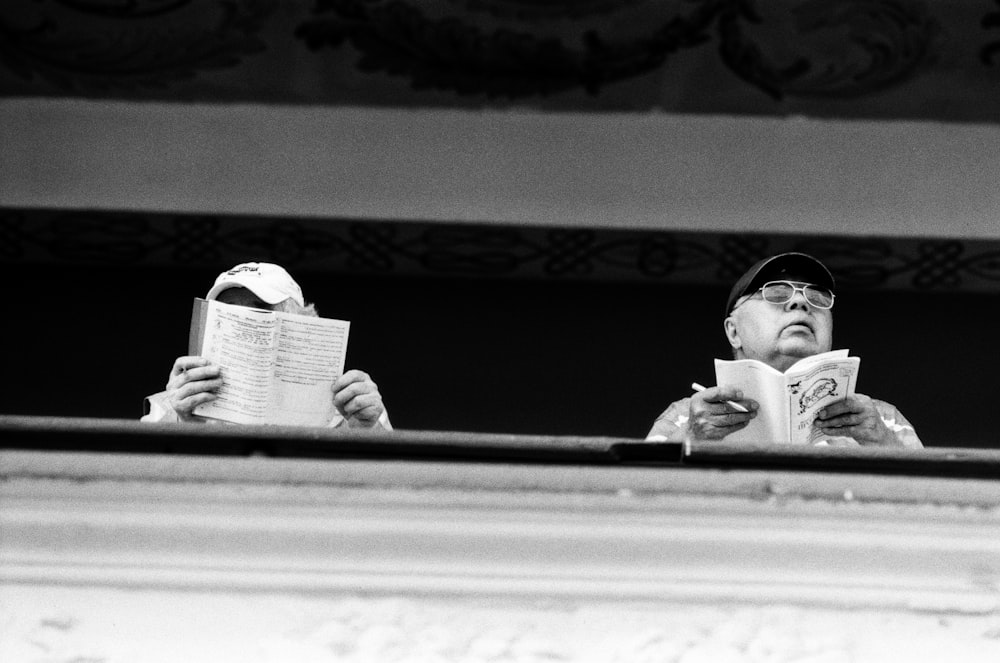 two men standing while holding books near railings