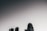 A skyline with a prominent modern skyscraper set against a gradient sky that transitions from dark grey to light grey. There is a linear object, possibly an airplane or shooting star, visible in the upper portion of the sky.